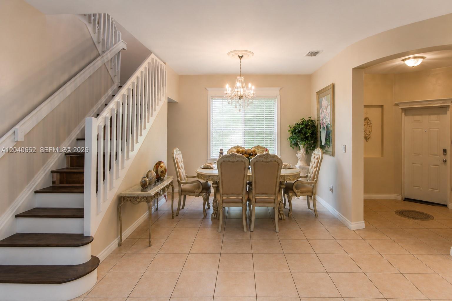 A dining room features a chandelier, a wooden staircase, and tile flooring — 116 SE 22nd Ter, Homestead FL 33033, HOMESTEAD, FL