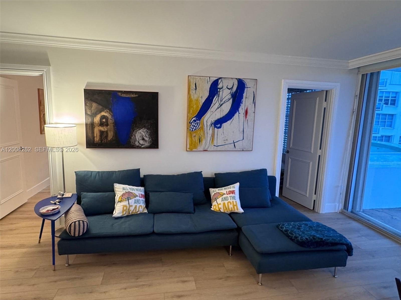 A living room features a blue sectional sofa, two abstract paintings, and a side table — 5151 Collins Ave # 436, Miami Beach FL 33140, MIAMI BEACH, FL