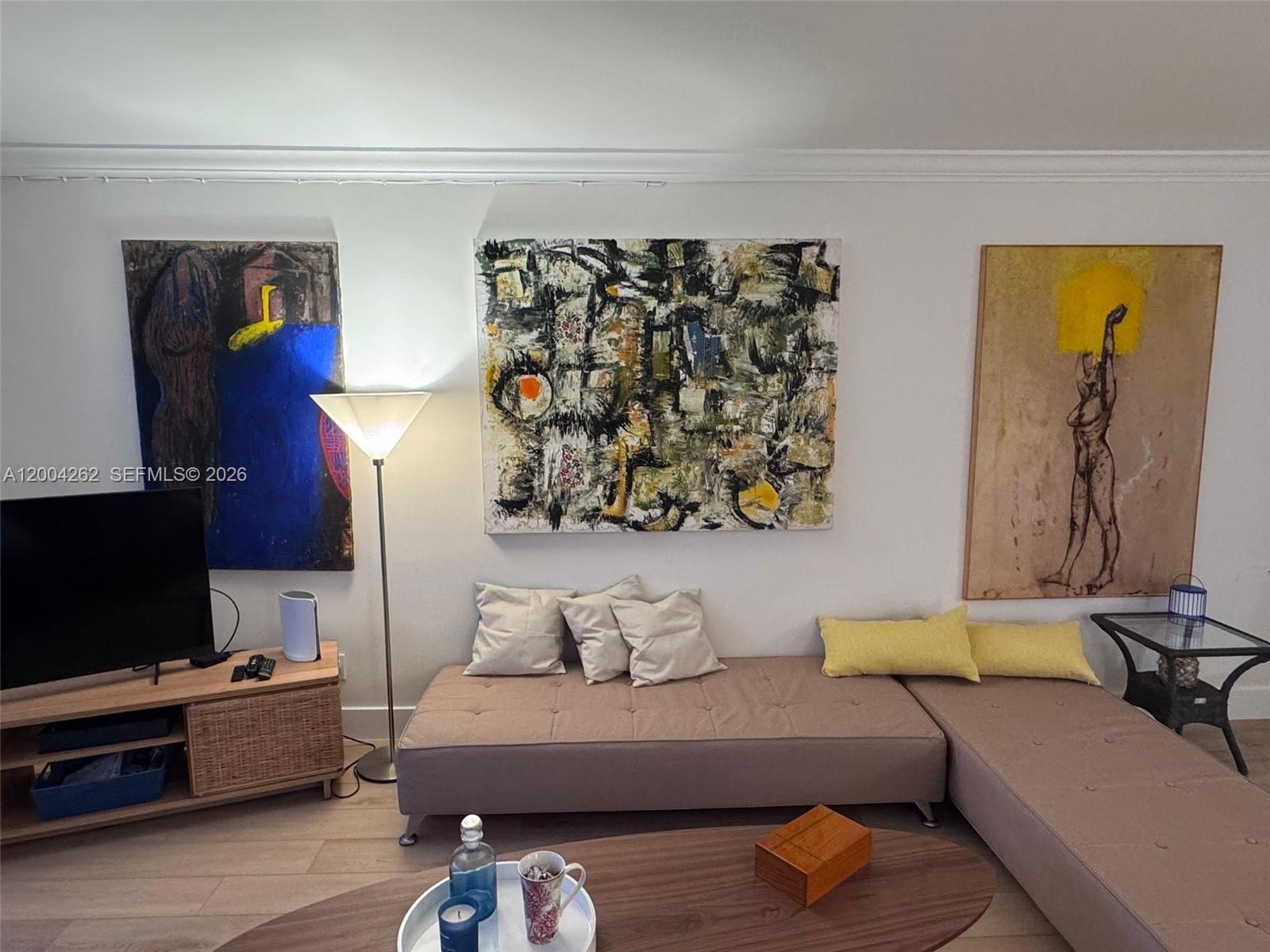 A living room features a sectional sofa, a coffee table, and three large abstract paintings — 5151 Collins Ave # 436, Miami Beach FL 33140, MIAMI BEACH, FL