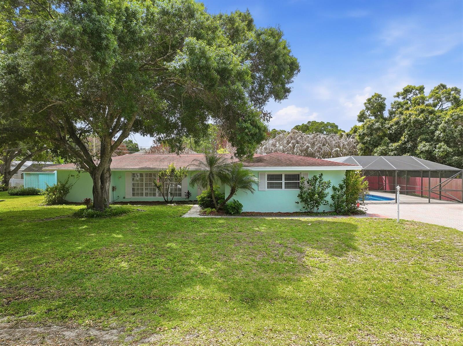 A light green, single-story house features a large front lawn, mature trees, and a pool — 2115 15th Place, Vero Beach FL 32960, VERO BEACH, FL