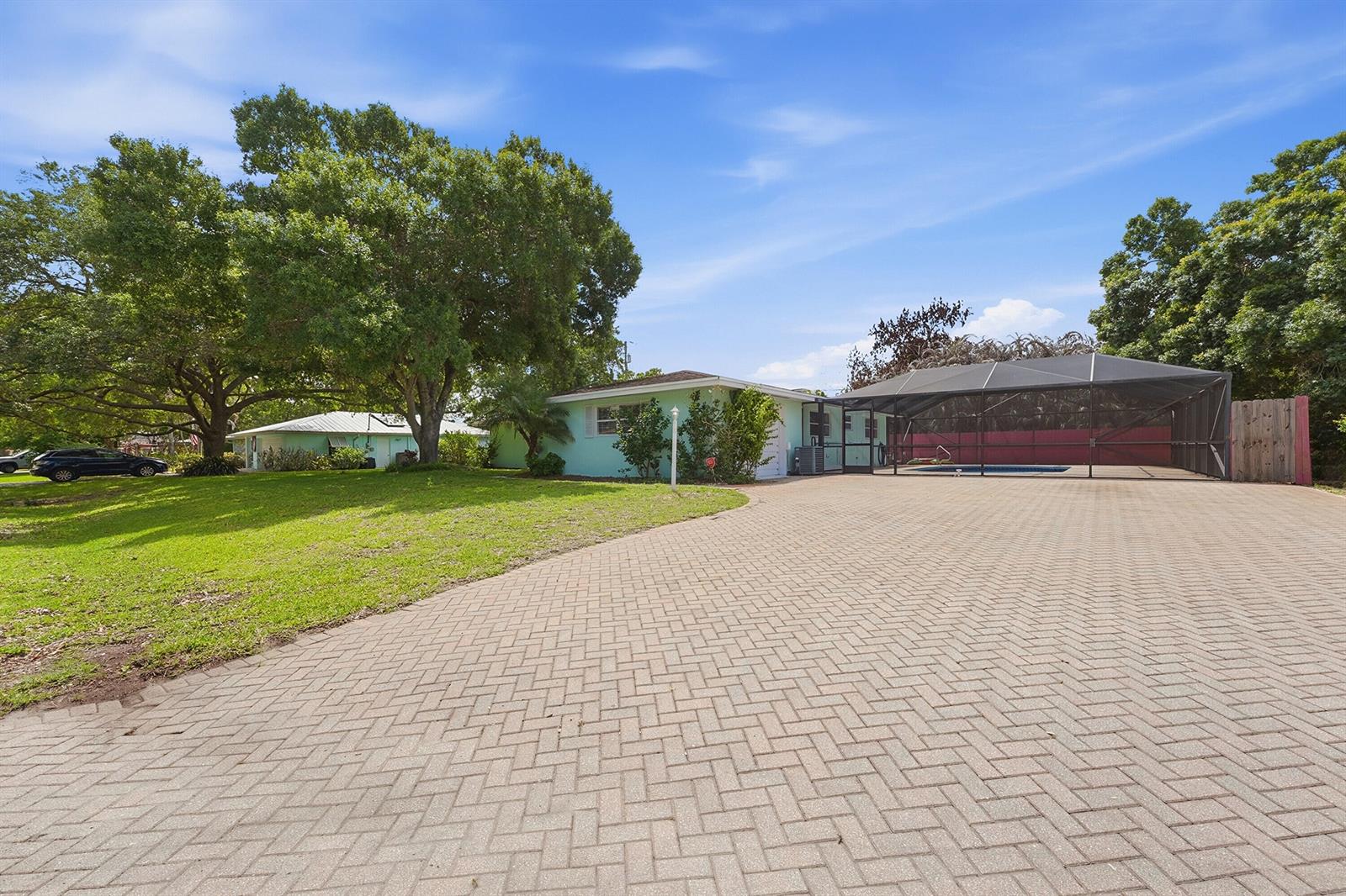A light green house features a large brick paver driveway and a screened-in pool area — 2115 15th Place, Vero Beach FL 32960, VERO BEACH, FL