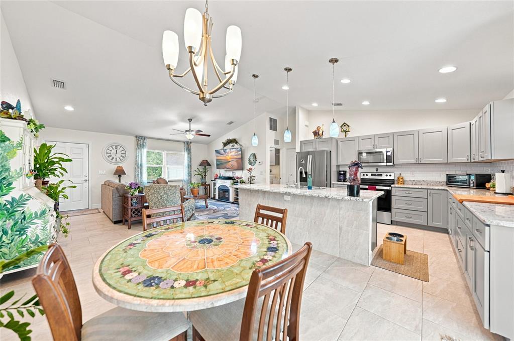An open-concept kitchen and dining area features light gray cabinets, granite countertops, and tile flooring — 5742 JANUS AVENUE, NORTH PORT, FL