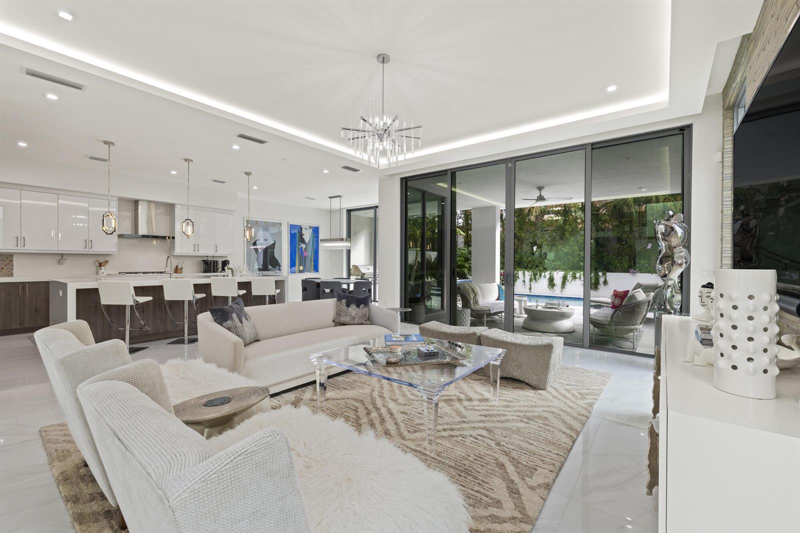 An open-concept living room and kitchen featuring a glass coffee table and sliding glass doors — 402 Ocean One Lane, Juno Beach FL 33408, JUNO BEACH, FL
