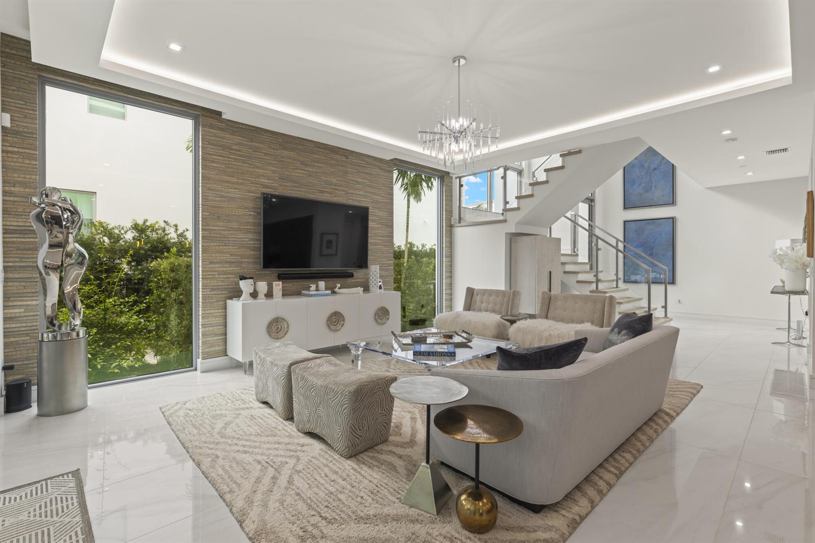 A modern living room features a textured accent wall, a glass staircase, and large windows — 402 Ocean One Lane, Juno Beach FL 33408, JUNO BEACH, FL