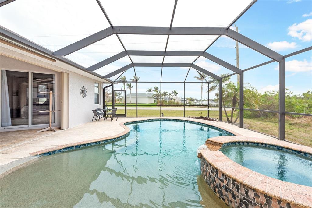 A screened-in patio features a swimming pool, a raised spa, and a tiled deck area — 8305 WELSFORD ROAD, PORT CHARLOTTE, FL