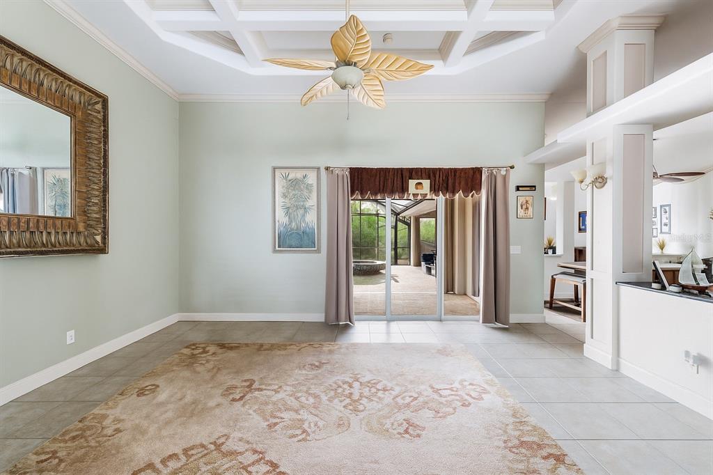 A living room with a coffered ceiling, leaf-shaped ceiling fan, tile floors, and sliding doors — 8305 WELSFORD ROAD, PORT CHARLOTTE, FL