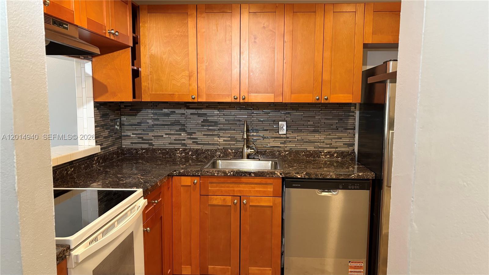 A kitchen features wood cabinets, dark granite countertops, a tiled backsplash, and stainless steel appliances — 4334 NW 9th Ave # 2F, Deerfield Beach FL 33064, DEERFIELD BEACH, FL