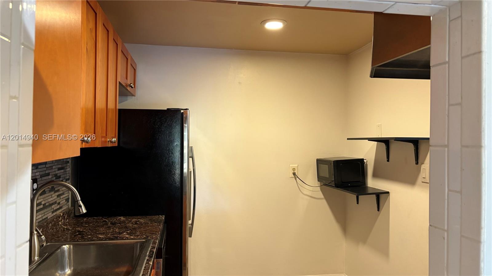 A kitchen features wood cabinets, a black refrigerator, a stainless sink, and wall-mounted shelves — 4334 NW 9th Ave # 2F, Deerfield Beach FL 33064, DEERFIELD BEACH, FL