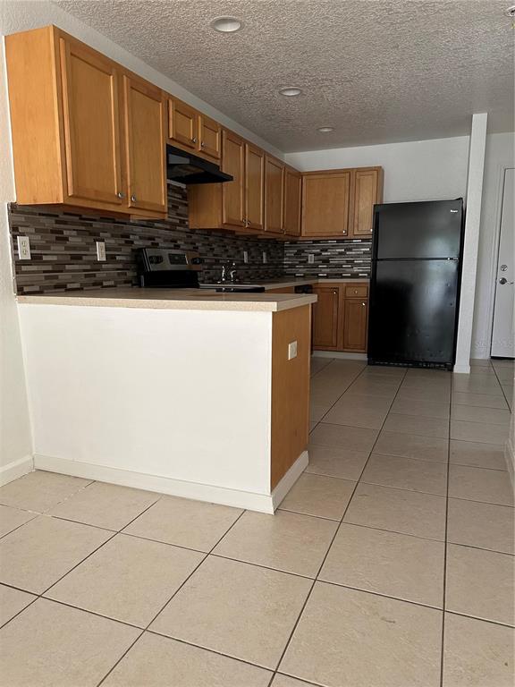 A kitchen features light wood cabinets, a tiled backsplash, and a black refrigerator — 752 E BROOME STREET UNIT 756, CLERMONT, FL