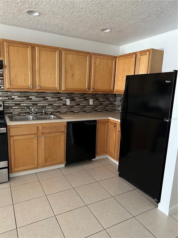 A kitchen features light wood cabinets, a black dishwasher, a black refrigerator, and tiled flooring — 752 E BROOME STREET UNIT 756, CLERMONT, FL