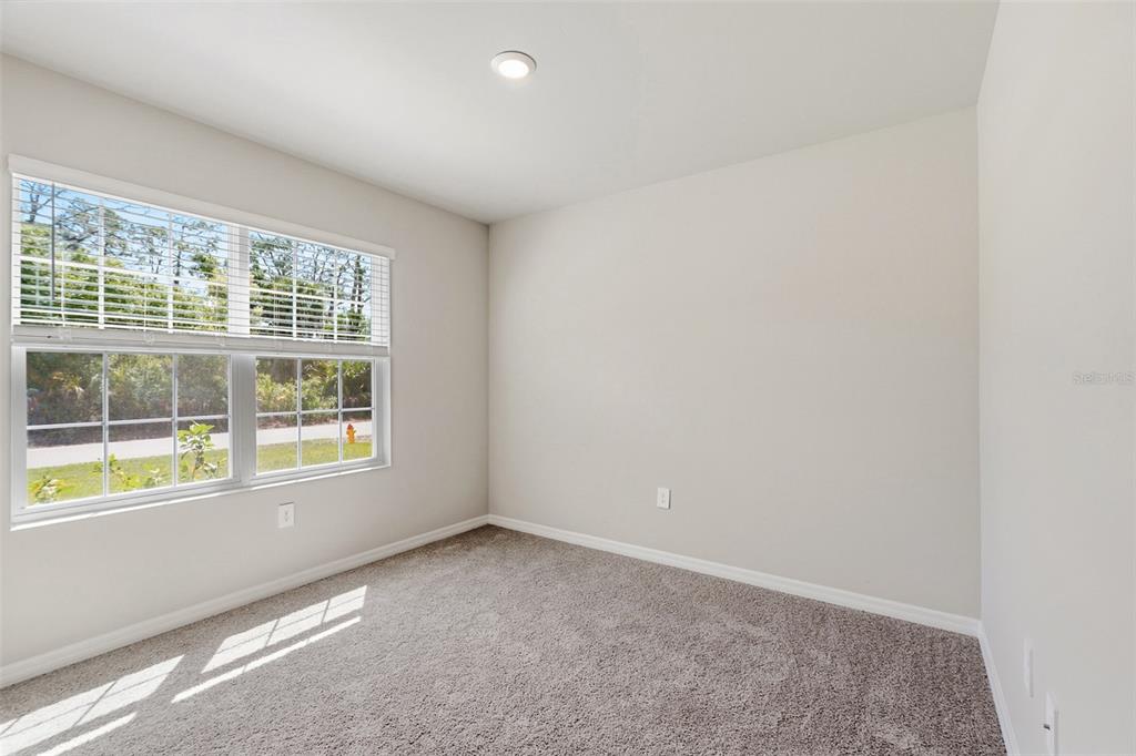 An empty bedroom features neutral walls, gray carpeting, and a window with white blinds — 25222 CADIZ DRIVE, PUNTA GORDA, FL