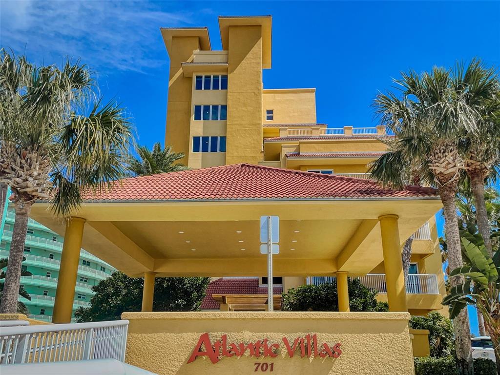 The exterior of the Atlantic Villas building features a yellow facade and a covered entrance — 701 N ATLANTIC AVENUE UNIT 401, NEW SMYRNA BEACH, FL