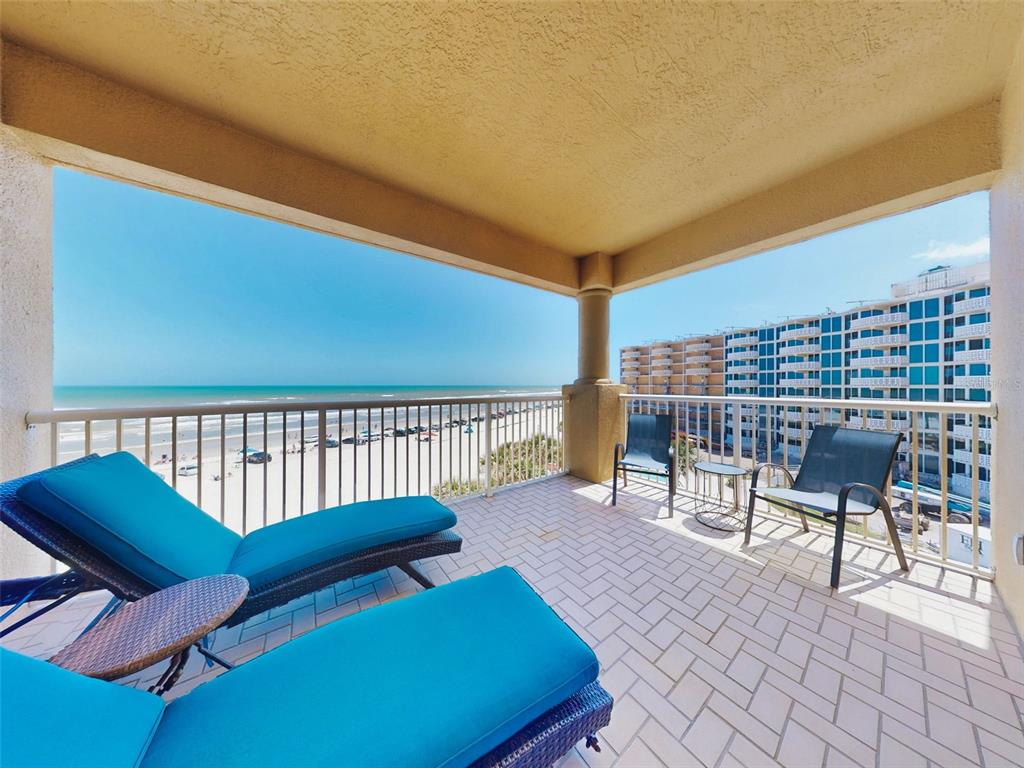 A covered balcony features blue lounge chairs, patio seating, and a view of the beach — 701 N ATLANTIC AVENUE UNIT 401, NEW SMYRNA BEACH, FL
