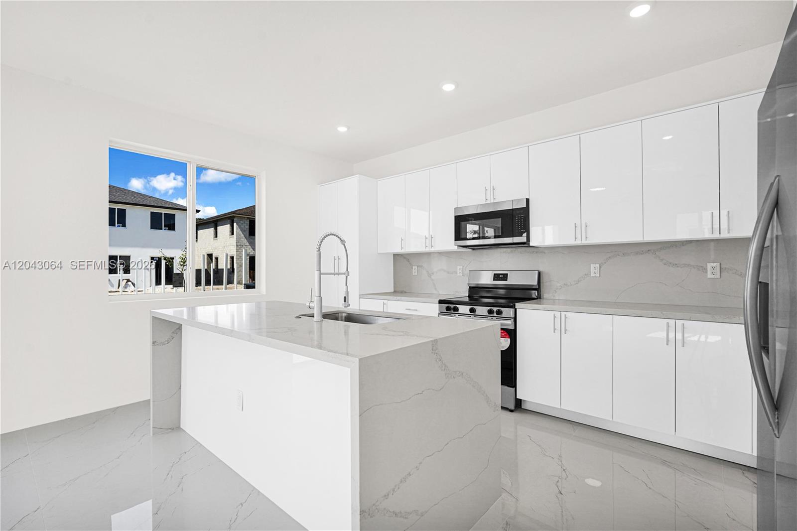 A modern kitchen features white glossy cabinets, a quartz island, and light-colored tile flooring — 22555 SW 125th Ave # 13A, Miami FL 33170, MIAMI, FL