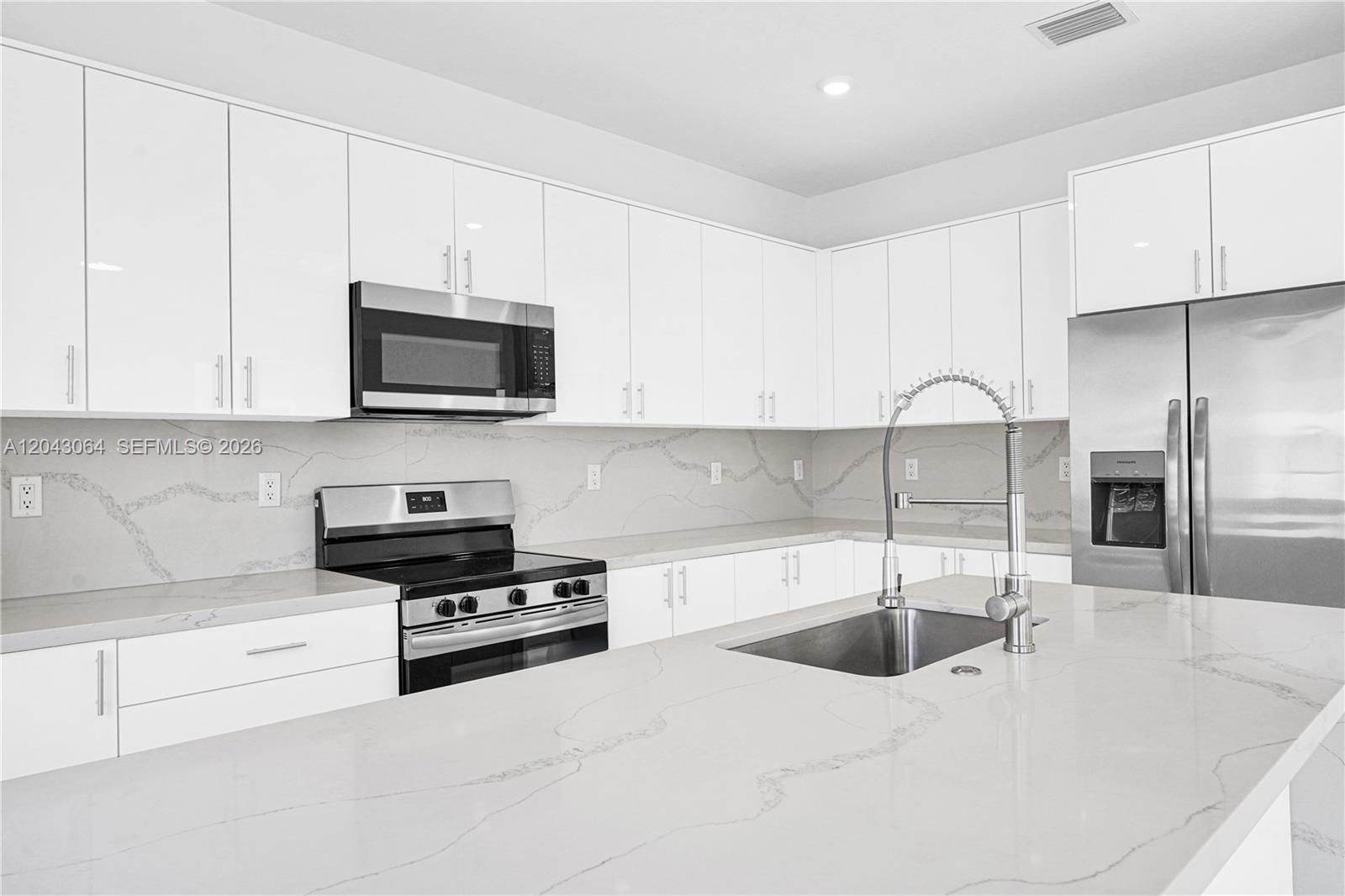 A modern kitchen features white cabinetry, stainless steel appliances, and a marble-patterned quartz countertop island — 22555 SW 125th Ave # 13A, Miami FL 33170, MIAMI, FL