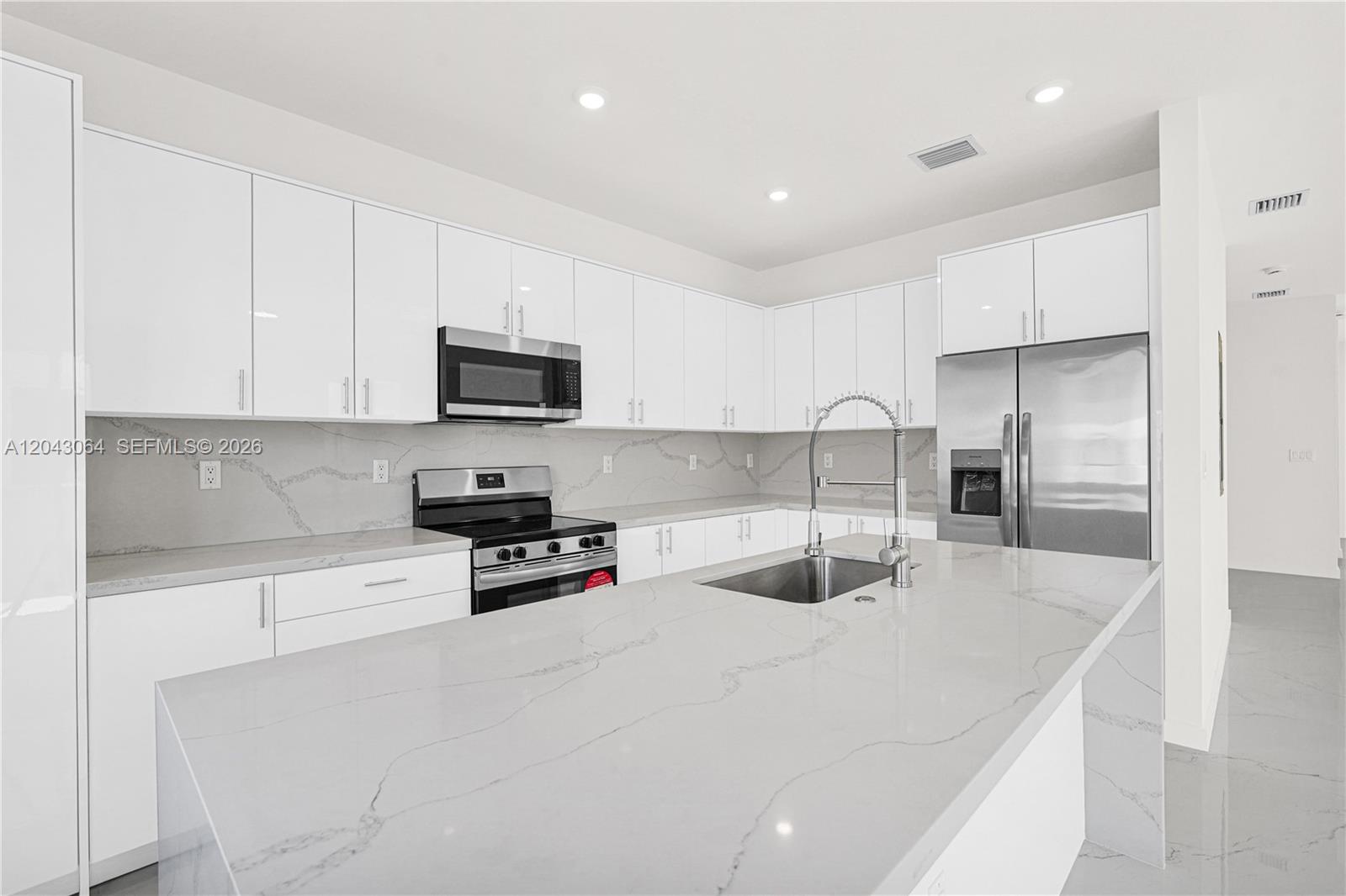 A modern kitchen features white cabinets, stainless steel appliances, and a large quartz island — 22555 SW 125th Ave # 13A, Miami FL 33170, MIAMI, FL