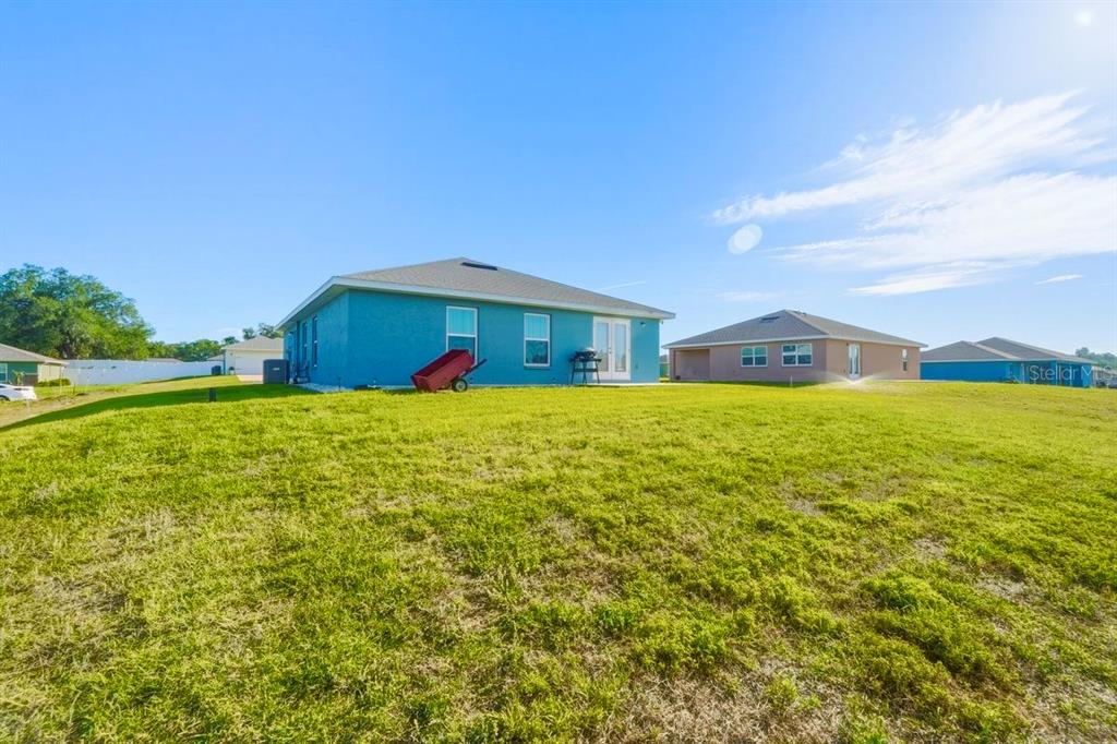 The rear exterior of a blue house with a large grassy yard and neighboring homes — 4447 E TAPER STREET, INVERNESS, FL