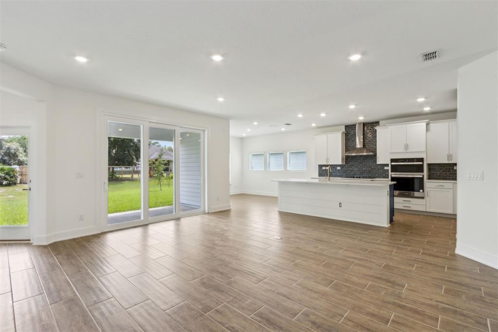 An open-concept kitchen and living area features wood-look tile flooring, white cabinetry, and sliding doors — 96100 Pirates Bluff Road, FL 32097, FL