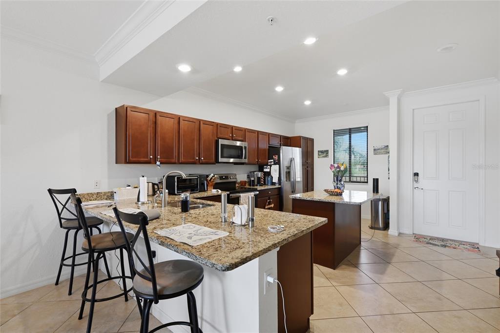 A kitchen with wood cabinets, granite countertops, a center island, and two bar stools — 16904 VARDON TERRACE UNIT 205, LAKEWOOD RANCH, FL