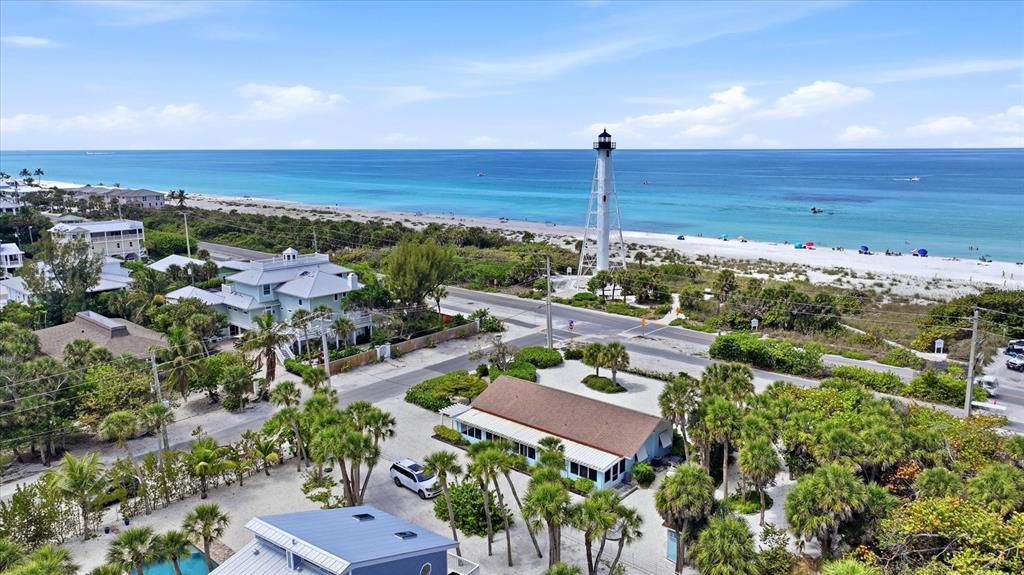 An aerial view shows a lighthouse near a beach, coastal homes, and lush tropical vegetation — 201 WHEELER ROAD, BOCA GRANDE, FL