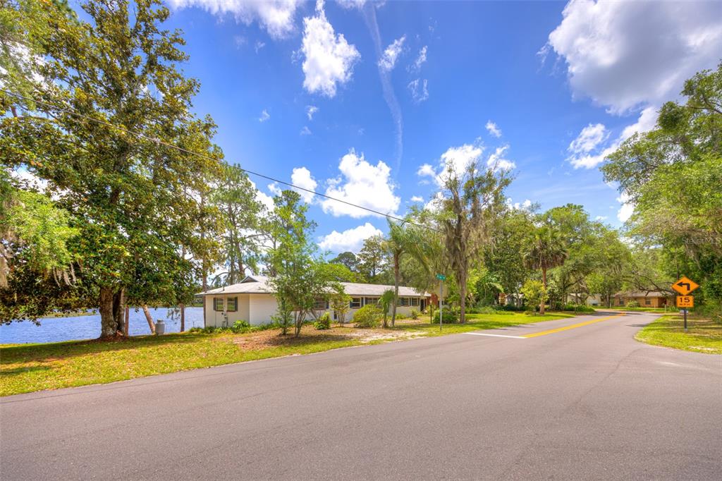 A single-story house sits beside a lake along a paved road with a speed sign — 33 WILLOW LANE, DELAND, FL