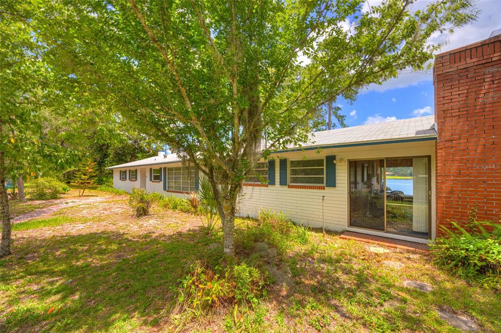 A white brick house with a red brick chimney and sliding glass doors faces a lake — 33 WILLOW LANE, DELAND, FL