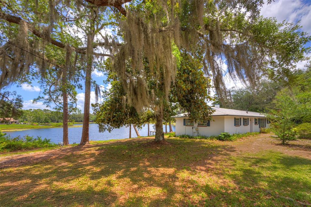 A white house sits on a grassy lot next to a lake under mossy trees — 33 WILLOW LANE, DELAND, FL