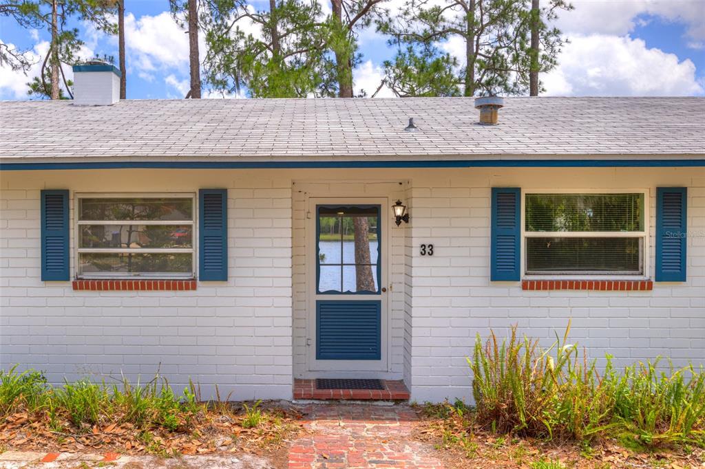 A white brick house exterior features a front door, blue shutters, and a shingled roof — 33 WILLOW LANE, DELAND, FL