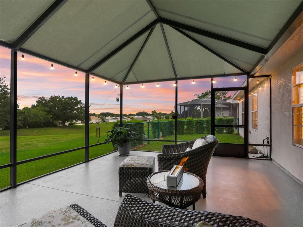 A screened-in patio features wicker furniture, a small fire pit, and a view of a lawn — 12211 SE 175TH LOOP, SUMMERFIELD, FL
