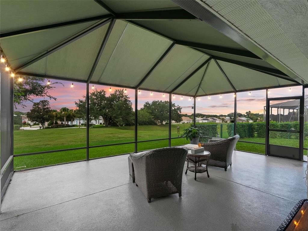 A screened-in patio features wicker furniture and a view of a grassy backyard at sunset — 12211 SE 175TH LOOP, SUMMERFIELD, FL
