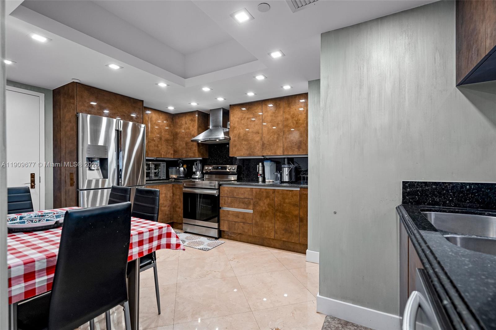 A kitchen features brown wood cabinetry, stainless steel appliances, and a dining table with chairs — 9559 Collins Ave # F, Surfside FL 33154, SURFSIDE, FL