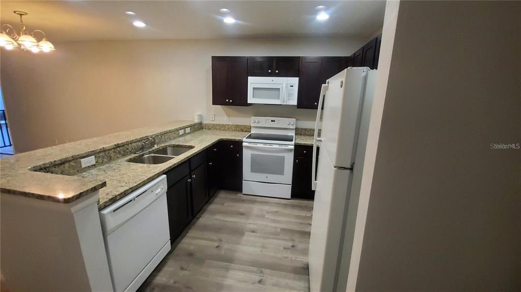 A kitchen features dark wood cabinets, granite countertops, white appliances, and light wood-look flooring — 284 GARDNER LANE UNIT F, KISSIMMEE, FL