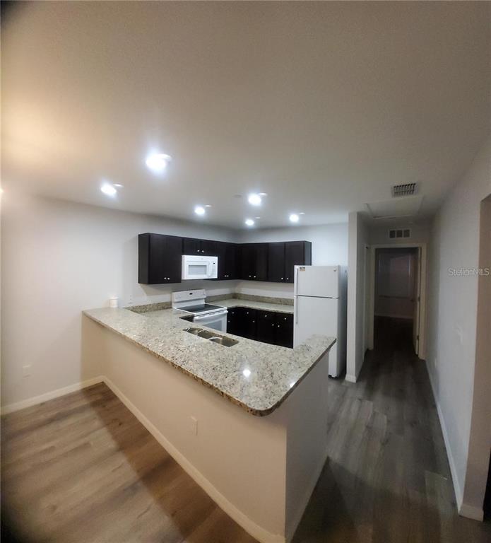 A kitchen features dark cabinets, granite countertops, a white refrigerator, and light wood-look flooring — 284 GARDNER LANE UNIT F, KISSIMMEE, FL