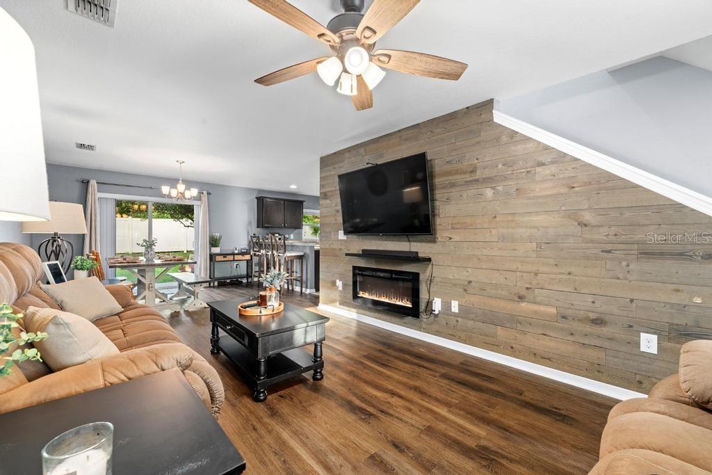 A living room features a wood-plank accent wall with a mounted television and electric fireplace — 10427 RIVERCREST DRIVE, RIVERVIEW, FL