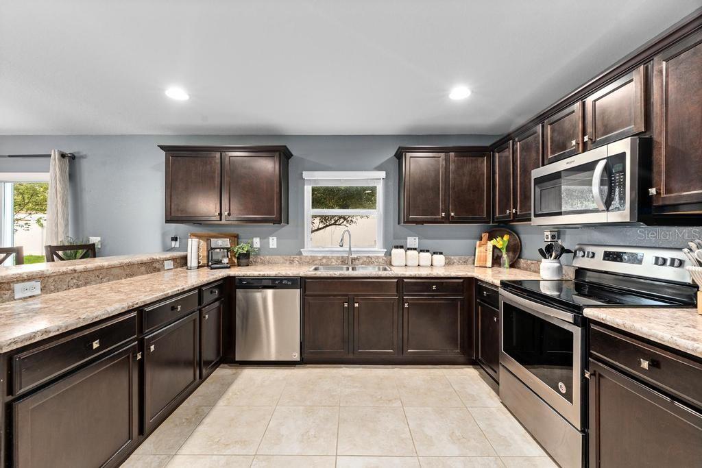 A kitchen with dark wood cabinets, granite countertops, stainless steel appliances, and tile flooring — 10427 RIVERCREST DRIVE, RIVERVIEW, FL