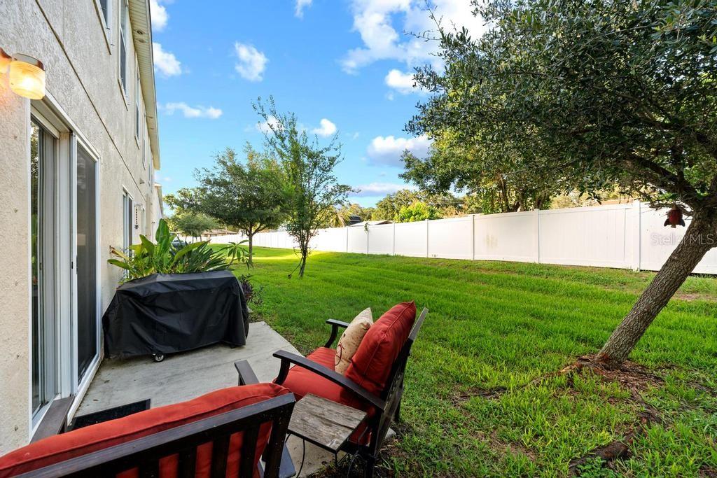 A backyard patio features two red chairs, a covered grill, and a white privacy fence — 10427 RIVERCREST DRIVE, RIVERVIEW, FL