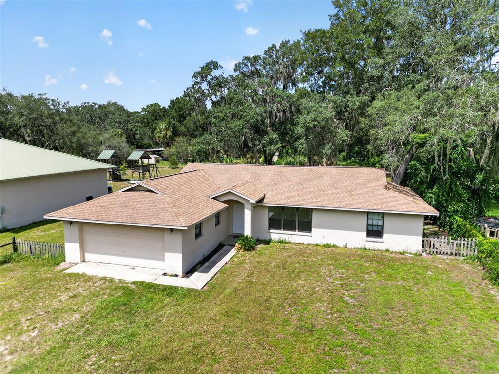 An exterior view of a single-story house with a tan roof and a two-car garage — 9590 SE 190TH COURT, OCKLAWAHA, FL