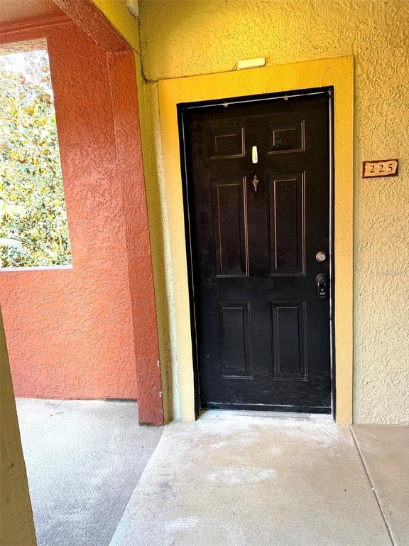 A black front door with a silver knocker is set in a yellow stucco wall — 1325 ROTONDA POINT UNIT 225, LAKE MARY, FL