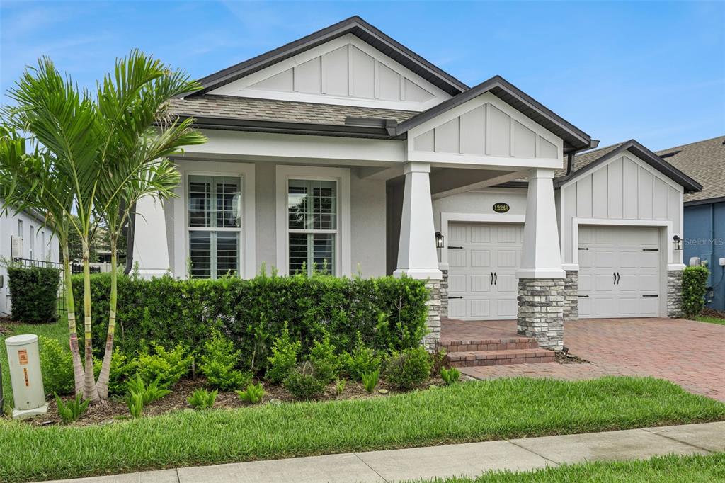 A single-story house with a stone-accented porch, two garage doors, and a manicured hedge — 12248 ENCORE AT OVATION WAY, WINTER GARDEN, FL
