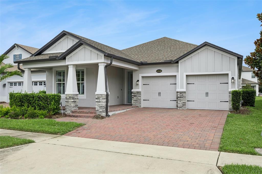 A single-story house with a brick driveway, two-car garage, and a covered front porch — 12248 ENCORE AT OVATION WAY, WINTER GARDEN, FL