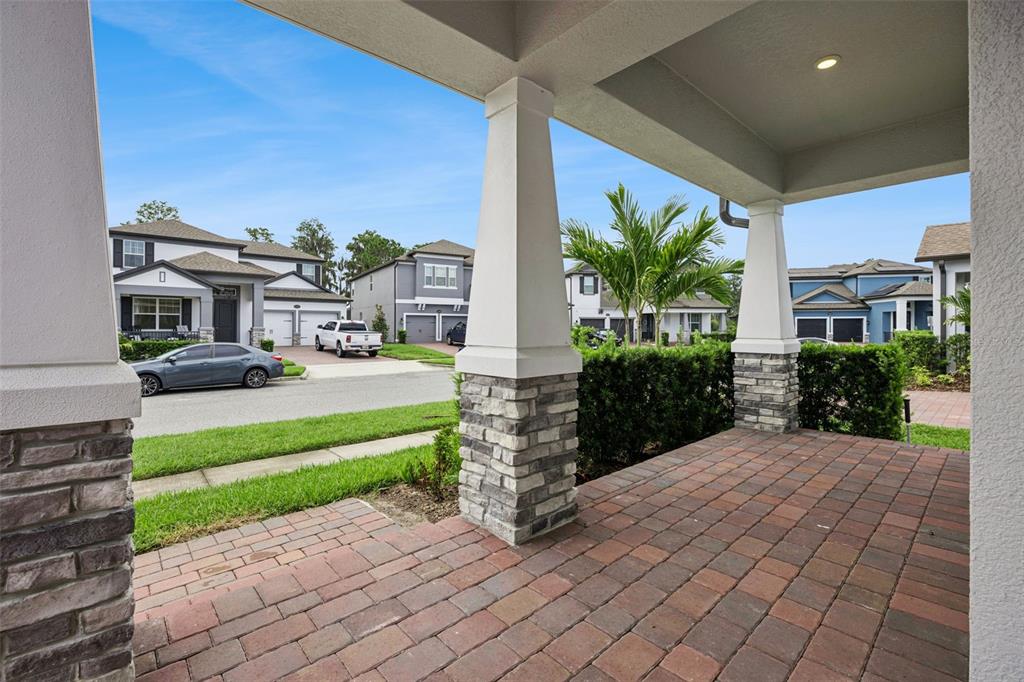 A covered brick porch features stone-based columns overlooking a suburban street with houses and cars — 12248 ENCORE AT OVATION WAY, WINTER GARDEN, FL