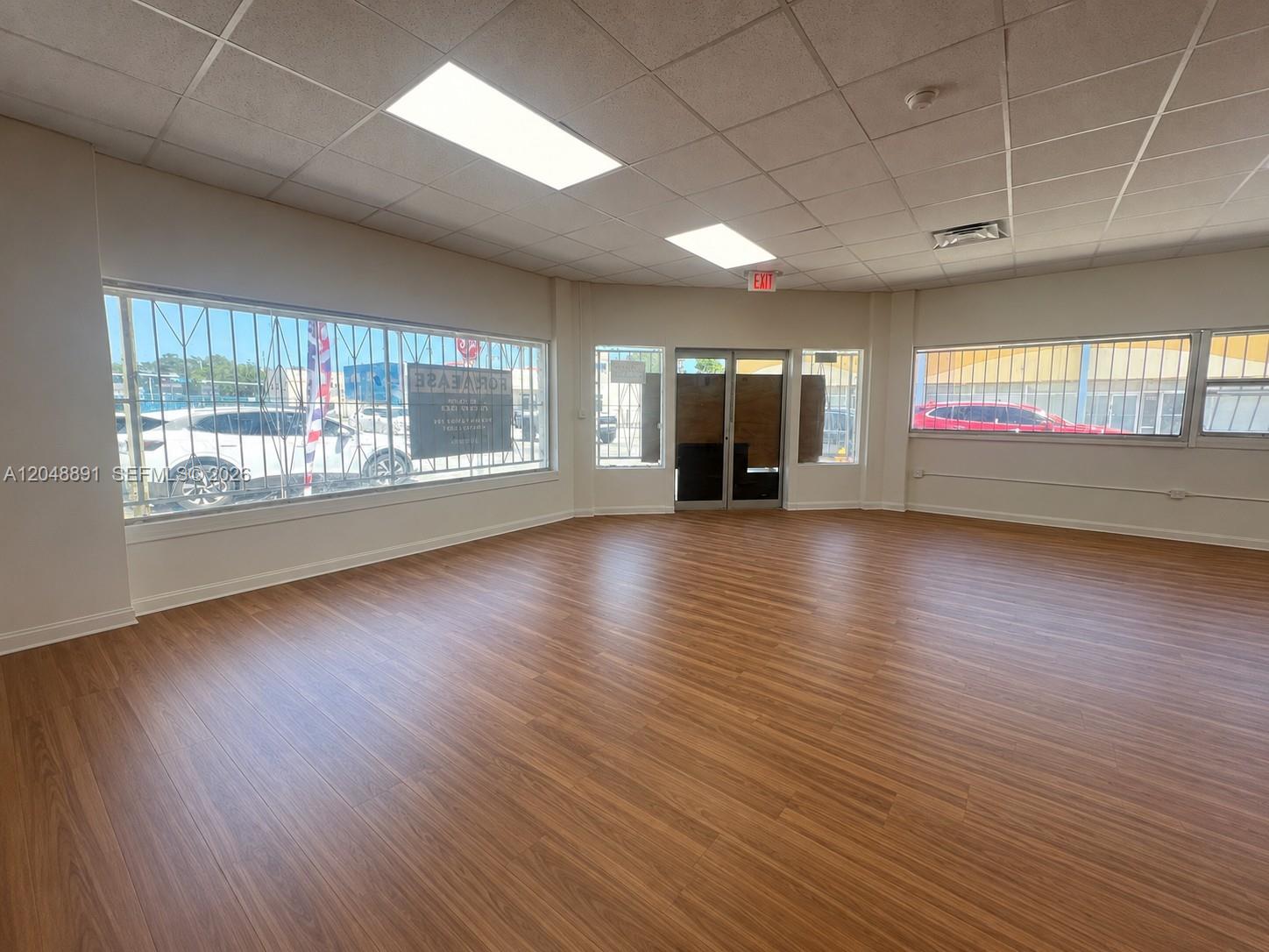 An empty commercial space features wood-look flooring, large windows with security bars, and drop ceilings — 2601 W Flagler St, Miami FL 33135, MIAMI, FL