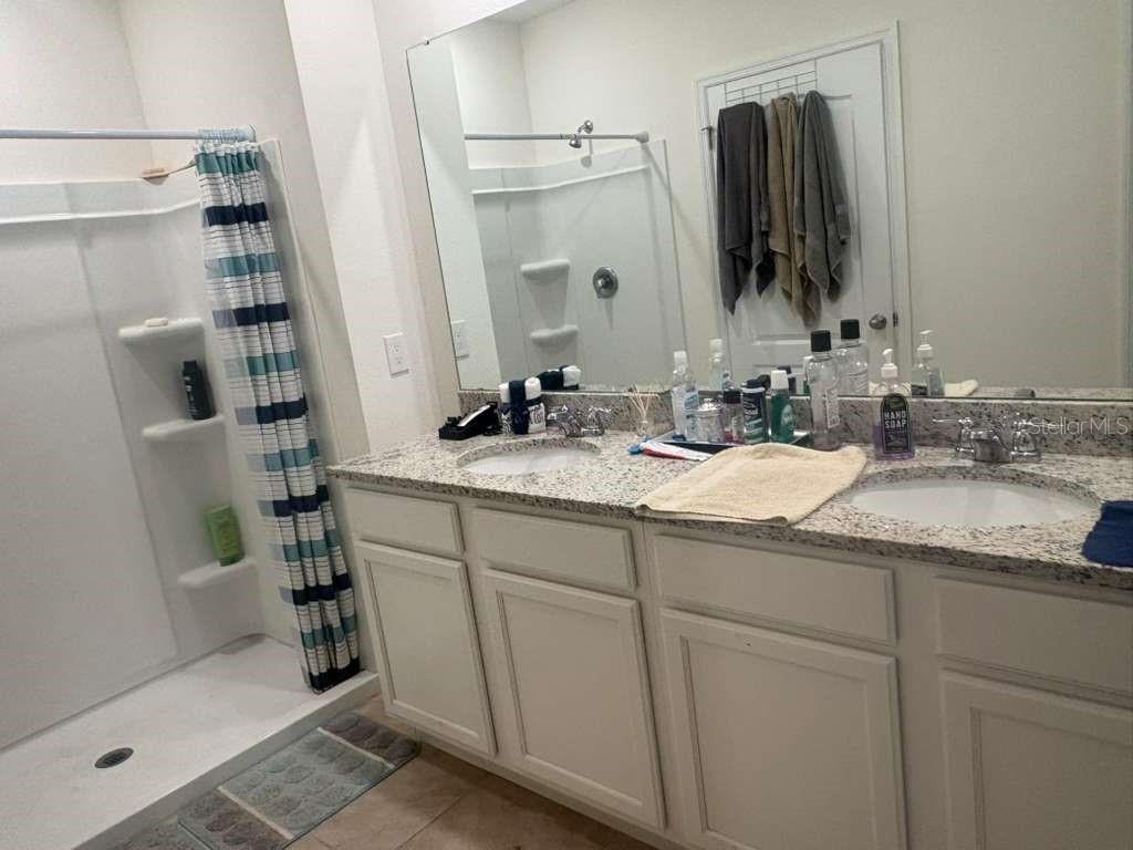 A bathroom features a double vanity with granite countertops, white cabinets, and a walk-in shower — 2343 AQUILINE NEST STREET, EAGLE LAKE, FL