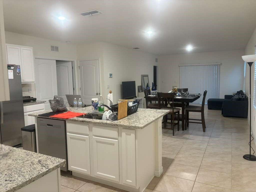 A kitchen with white cabinets and granite countertops opens to a dining and living area — 2343 AQUILINE NEST STREET, EAGLE LAKE, FL