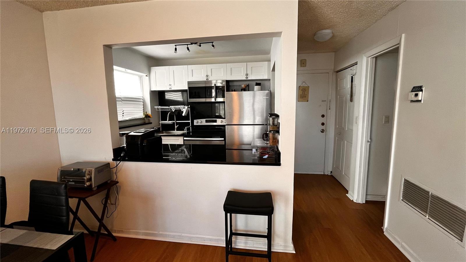 A kitchen with stainless steel appliances and white cabinets overlooks a dining area — 1990 Marseille Dr # 407, Miami Beach FL 33141, MIAMI BEACH, FL