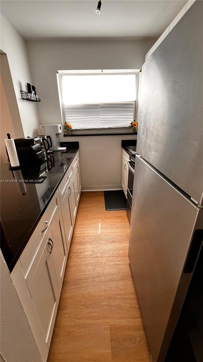 A narrow galley kitchen features white cabinets, black countertops, and stainless steel appliances — 1990 Marseille Dr # 407, Miami Beach FL 33141, MIAMI BEACH, FL