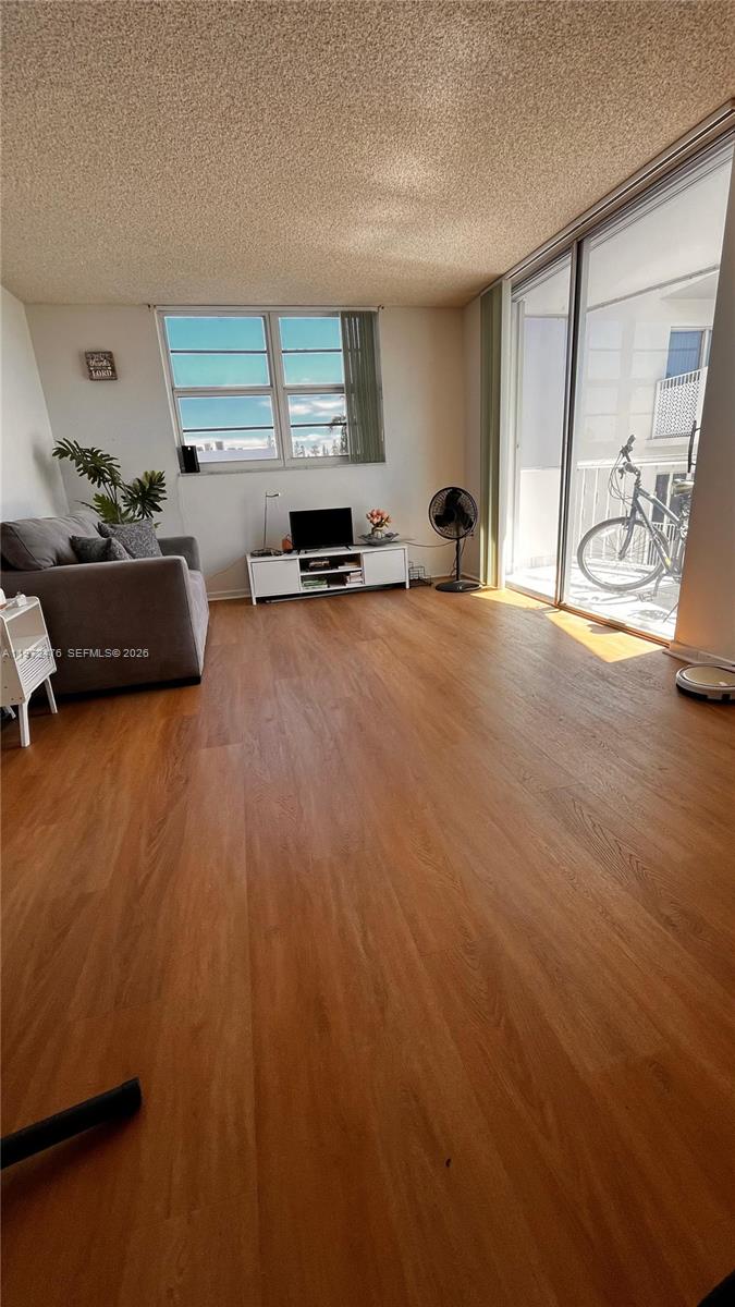 A living room features wood-look flooring, a gray sofa, a media console, and a balcony — 1990 Marseille Dr # 407, Miami Beach FL 33141, MIAMI BEACH, FL
