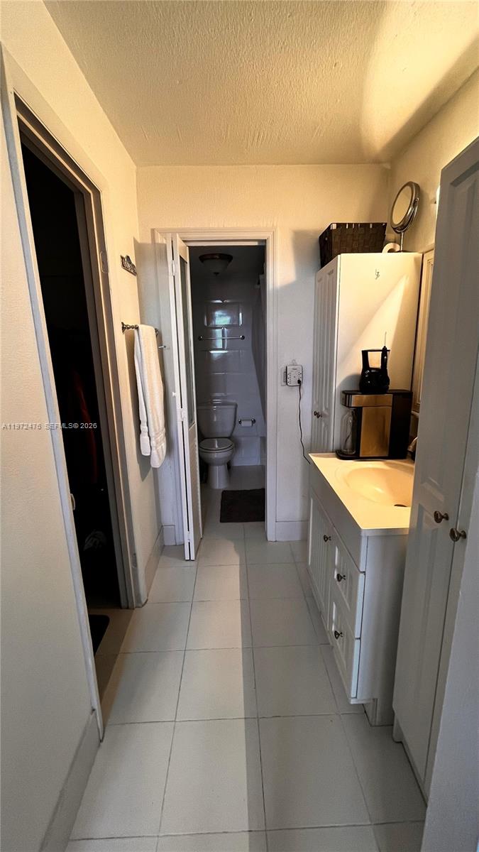 A bathroom features a vanity with a coffee maker, a toilet, and a closet door — 1990 Marseille Dr # 407, Miami Beach FL 33141, MIAMI BEACH, FL