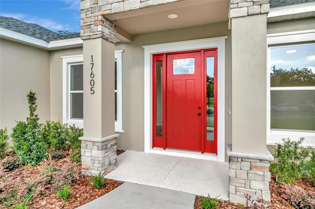 The front entrance of a house features a bright red door and stone-accented columns — 17605 NINTH STREET, MONTVERDE, FL