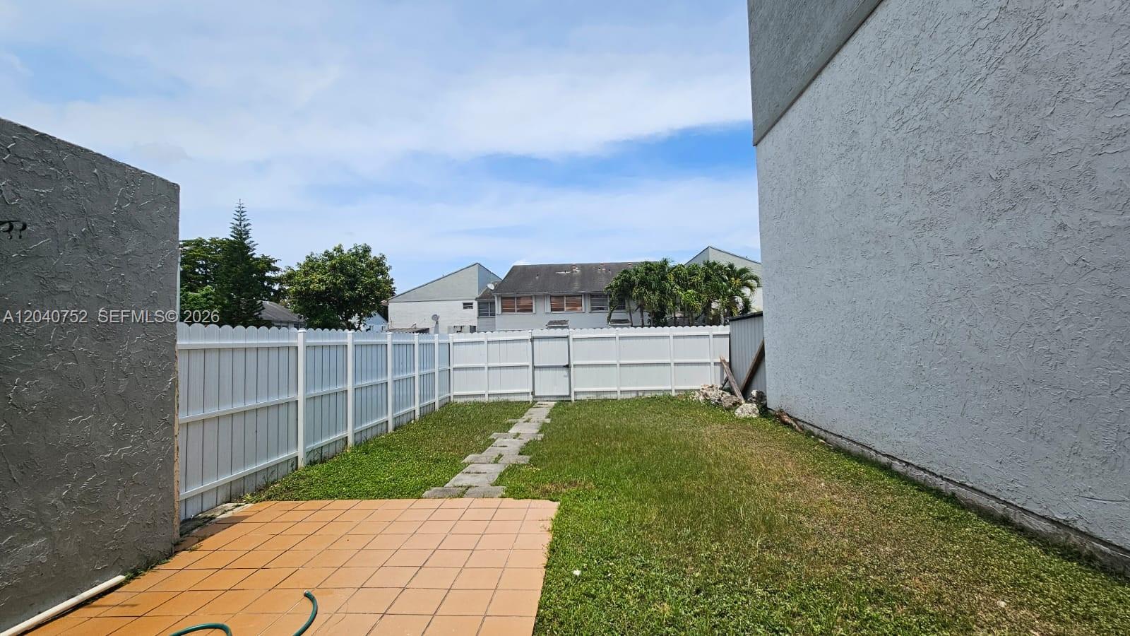 A fenced backyard features a tiled patio, a grass lawn, and a stone walkway — 8460 SW 156th Pl # 702, Miami FL 33193, MIAMI, FL